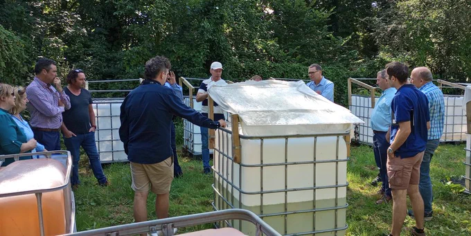 People standing around a duckweed growth setup, created from a IBC with a cover to give shelter from rain and too bright sunshine.