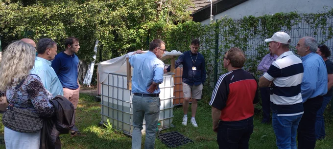 People gathered around the duckweed growth tank outside. The tank is made from an IBC with a perspex and cheesecloth cover to protect from rain and direct sunlight. 