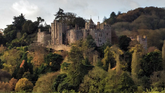 A long shot of Dunster Castle in early autumn, the castle stands on a wooded hill with some of the trees turning autumnal colours. 