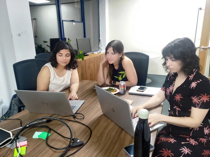 three women with laptops seated around a meeting room table