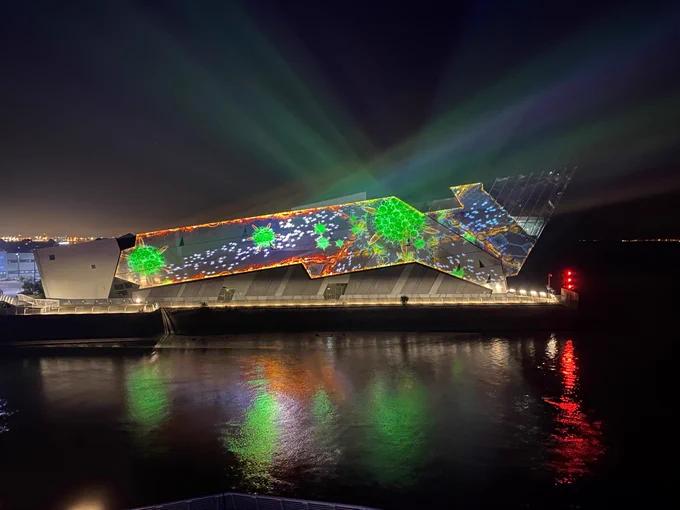 The side of The Deep building illuminated with bright green shapes and lights. The building is overlooking the Humber Estuary. 