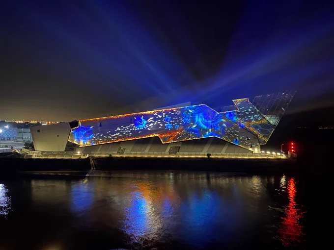 The side of The Deep building illuminated with bright blue shapes and lights. The building is overlooking the Humber Estuary. 