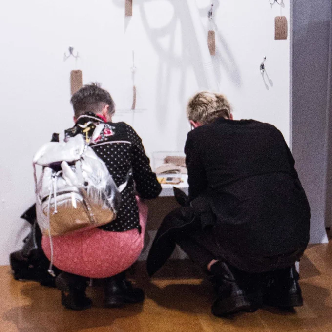 View from behind of two people bending over to examine a display case in an exhibition. 