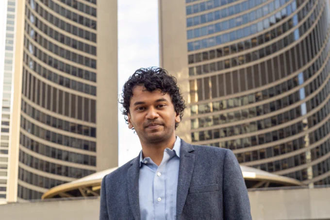 Kevin standing in fronto Toronto City Hall wearing a light blue dress shirt and a blazer