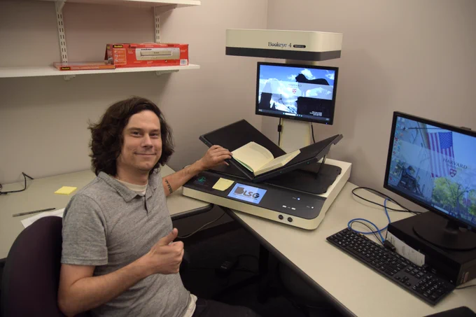 Ryan smiles at the camera while scanning a book on the scanner. Ryan is giving a thumbs up.