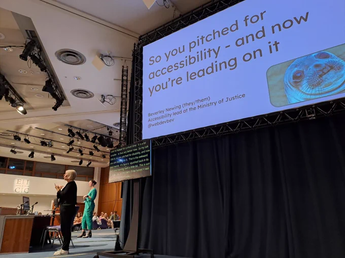 Bev on stage with signer caption display and slide sceen