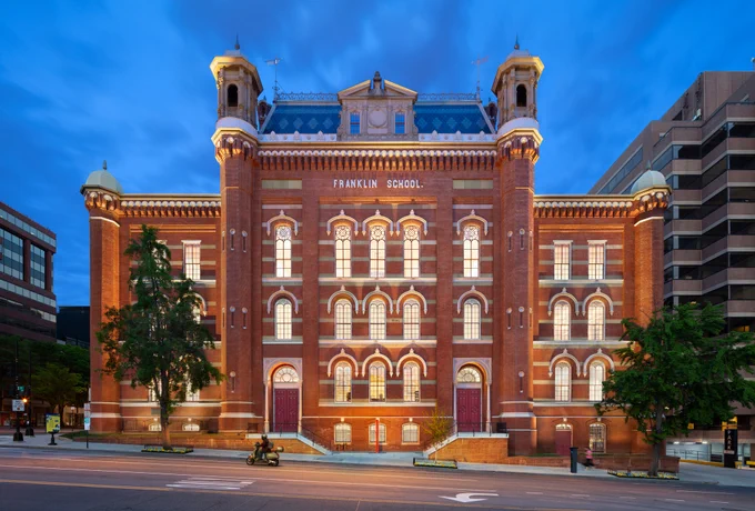 The Planet Word building at night. It is a historic red brick building with decorative windows, cupolas, and a mansard roof.