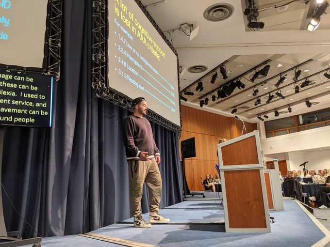 Craig stood on the Accessibility Scotland stage, facing the audience, with his slides behind him a big screen