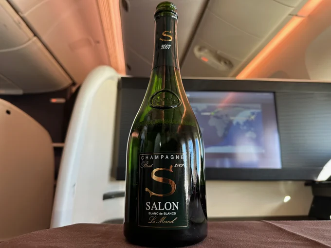 A bottle of Salon Champagne sits on the table of a Japan Airlines first class seat.