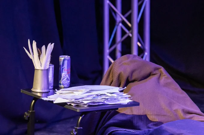A desk, littered with papers, tankards, Red Bull cans and a blanket.