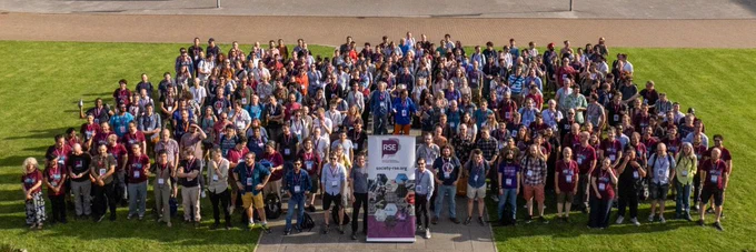 Conference photo showing 300  attendees standing in a big square outside on the grass looking up at a drone camera.