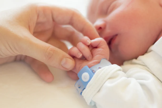 A woman's hand caresses the hand of a newborn.