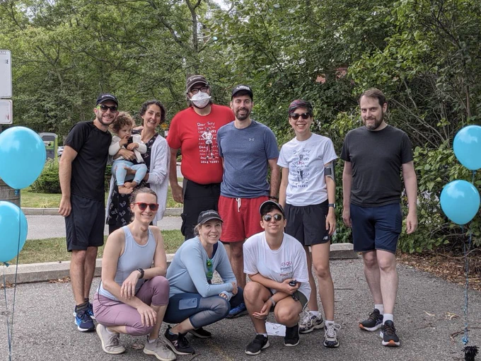 Nine Countermeasure members and a baby in workout clothes, ready for the Terry Fox Run, surrounded by teal balloons