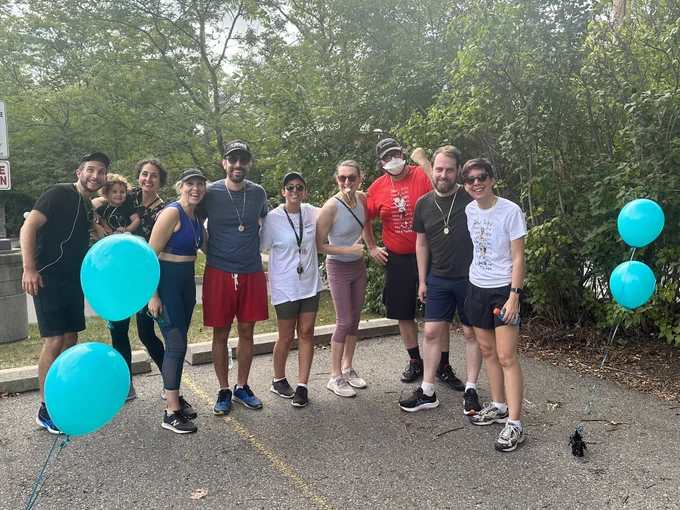 Nine Countermeasure members and a baby in workout clothes, sweaty and tired but triumphant after finishing the Terry Fox Run, surrounded by teal balloons