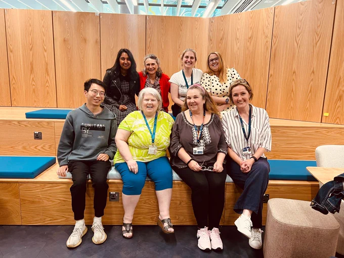 Eight people sitting and posing for a photo. Four people - an East/Southeast Asian man and three white women - sitting in the front row. And Four people - an Asian women and three white women - sitting the the back row.