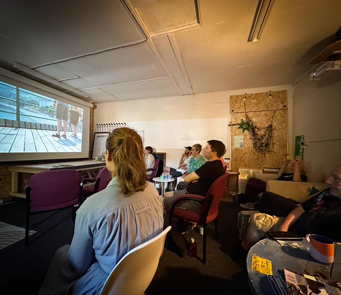 a group are sitting and watching a pull down cinema screen