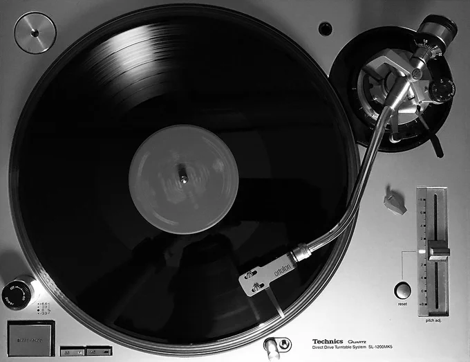Overhead view of a black vinyl record on a silver Technics turntable with the needle two tracks in on the record.