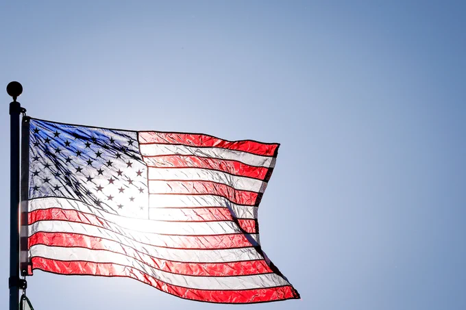 The American flag waving in the wind with the sun in the background. 