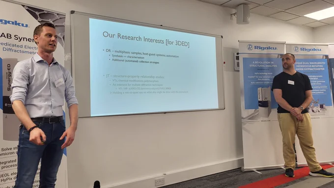 Daniel Rainer (on the left) and Jere Tidey (on the right) flank a presentation slide where some of their scientific interests are listed. 
