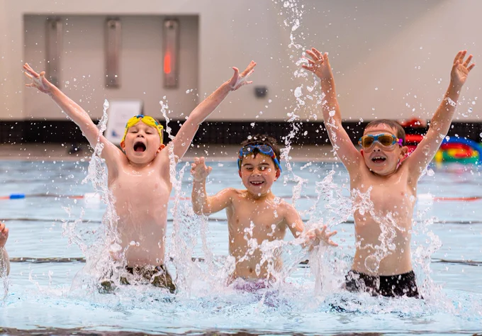 3 children splashing in a swimming pool.