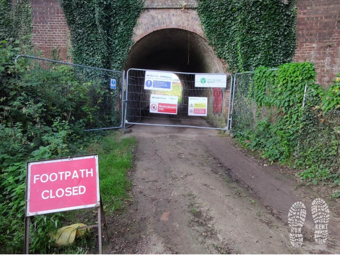 Fenced off footpath under a railway bridge, with a sign saying 'footpath closed'