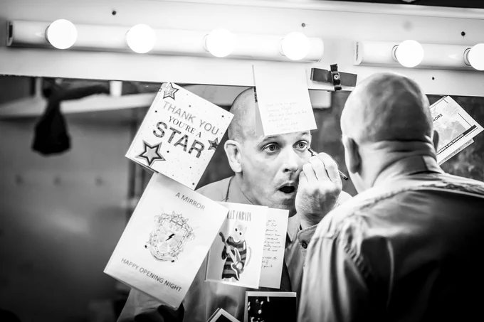 One actor looks in the mirror as he does his makeup