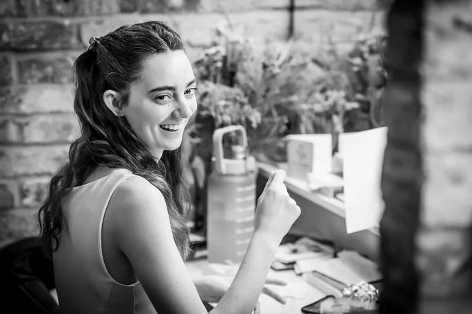 One actor smiles and sits in front of a mirror in a dressing room