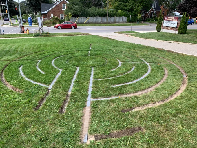 A circular labyrinth, made of paving stones set into a lawn, is being built. The most recently laid paving stones are covered in dirt and hard to see.