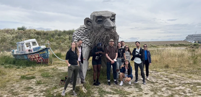A group of students and instructor John MacArthur standing near a large troll, which towers above them nearly twice their height. It has a long beard, a bald head, and a benign facial expression.