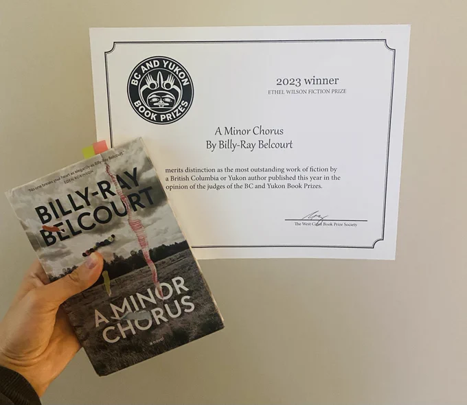 My hand holding a copy of the aforementioned novel and the award certificate
