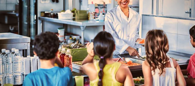 Three kids standing in lunch line waiting to be served food. 