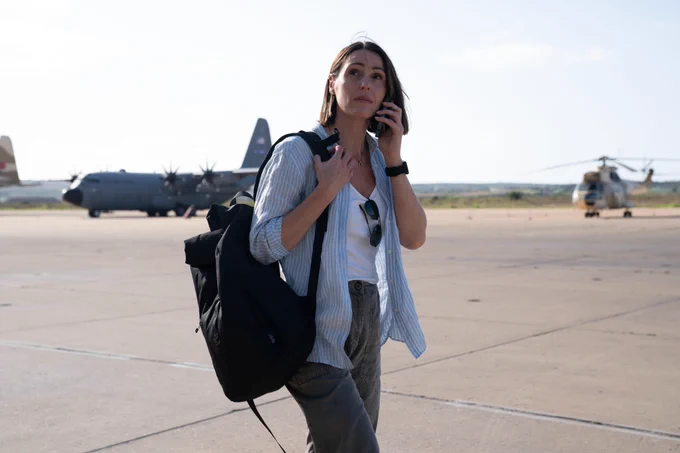 Amy Silva (Suranne Jones) stands on an airbase carrying a backpack. She appears to be on her phone.