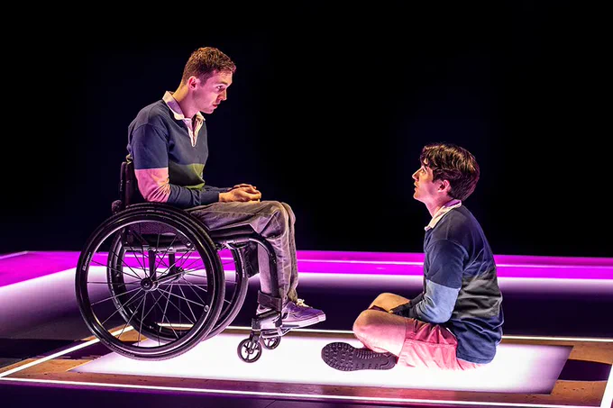 Ed Larkin, who is sitting in a wheelchair, and Jonny Amies, who is sitting cross-legged on the floor, in character as Henry Fraser
