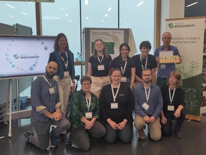 A group of people sitting and standing in front of the NFDI4Biodiverstiy booth at GfÖ2023.