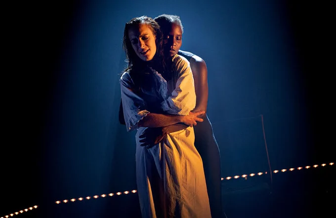 A performer wrapping their arms around another performers waist onstage 