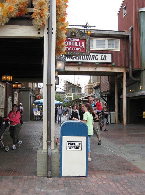 Tan and blue trash can labeled "Pacific Wharf" surrounded by guests at Disney California Adventure