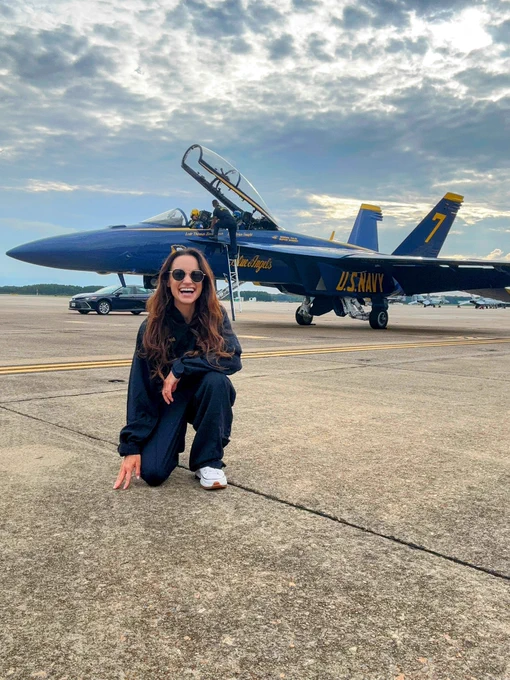 Emily in a flight suit kneeling in front of an F-18 on the runway
