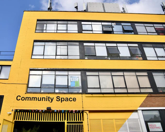Image of a yellow building with windows which has Community Space written above the door. 