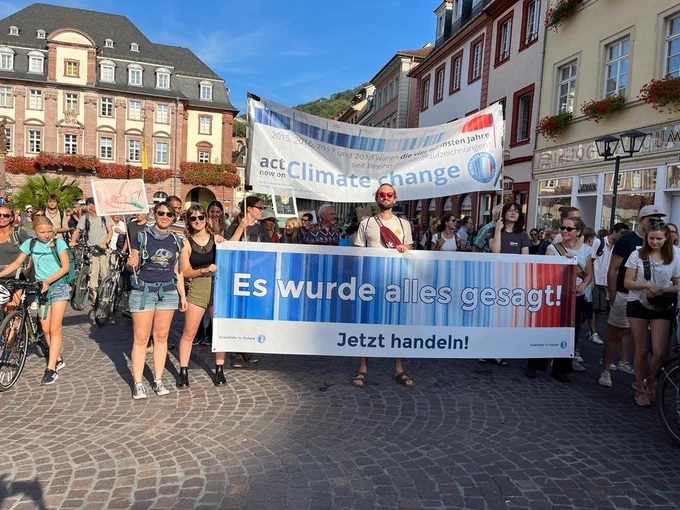 Foto des Klimastreik in Heidelberg
Im Vordergrund stehen die Scientists4Future und halten zwei Banner hoch. Darauf die Climate Stripes und der Text "Es wurde alles gesagt!" "Jetzt handeln!" 