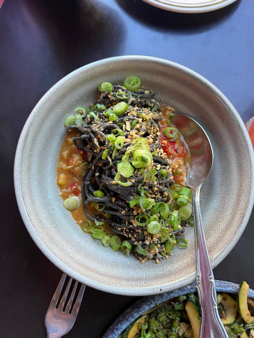 Bowl of squid ink noodles in a crab broth, topped with green onions.