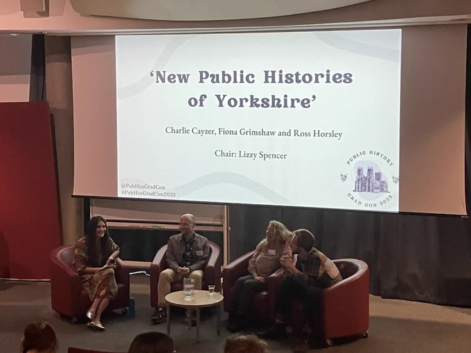 Four people sat on a stage below a large screen that says ‘New Public Histories of Yorkshire’