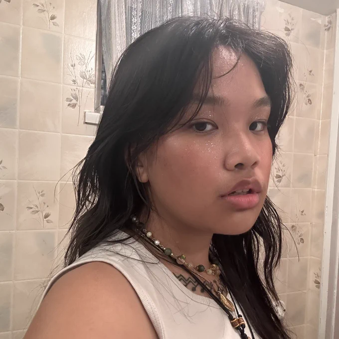 a selfie of anata laylay in front of a tiled wall with white curtains