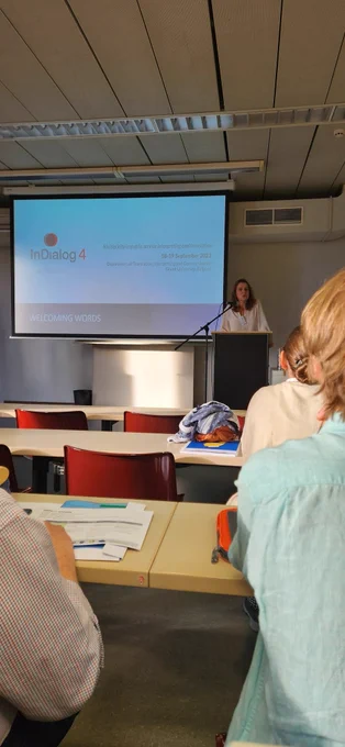 July stands at the lectern next to a PowerPoint projection