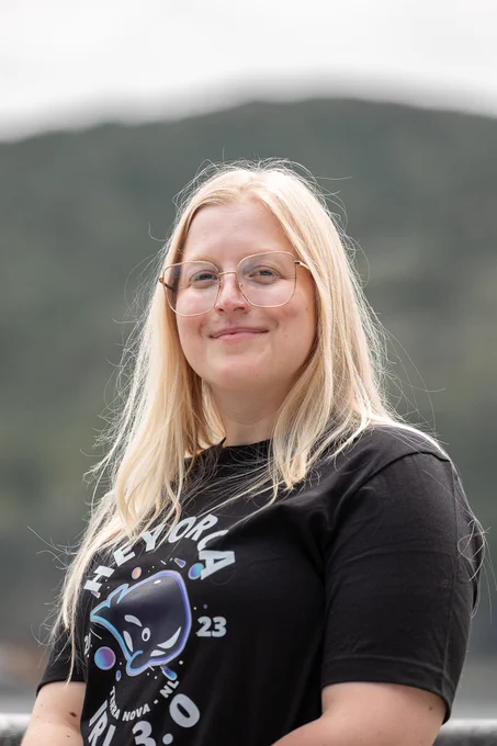 Stephanie Schwartz has long blonde hair and is wearing glasses and smiling. She is wearing a dark t-shirt with the HeyOrca logo, featuring a whale, printed on the middle.