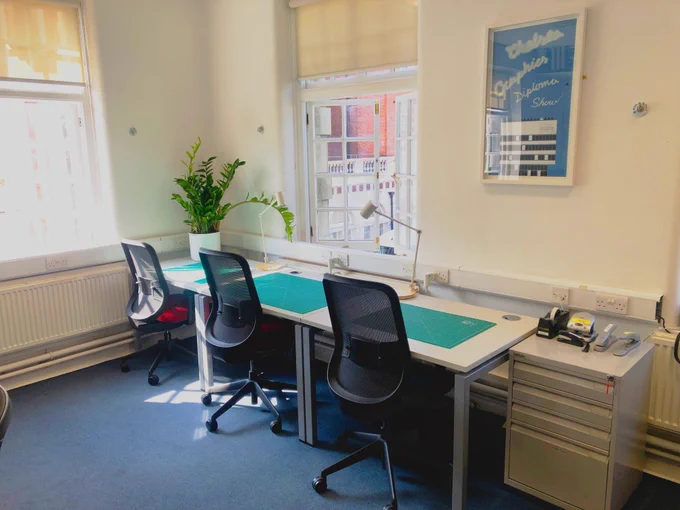 Cutting and glueing area in the Computer room at Chelsea Library. 3 desk chairs are sat at a long desk with green cutting mats and work lamps.