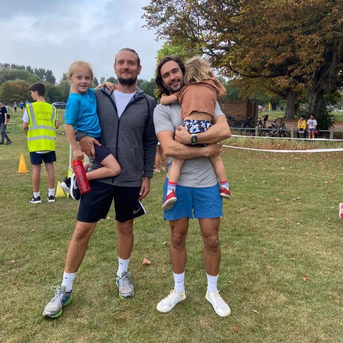 Picture of Joe Wicks and another man at junior parkrun with both of them holding their two children