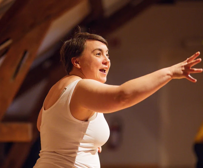 Stephe in performance, wearing a white vest. Her right arm is outstretched, and her face is animated.