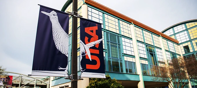 A view of a banner with the Rowdy Statue on it. In the background, the Student Union looms. 