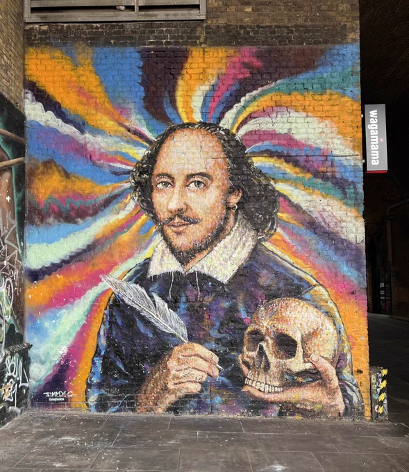 The Shakespeare mural on Southbank, with a portrait of Shakespeare holding a quill and skull on a colourful background of hues of blue, black, white, pink and orange.