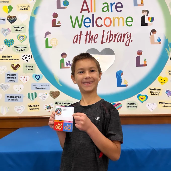 Boy standing in library and smiling. Holding up a prize.